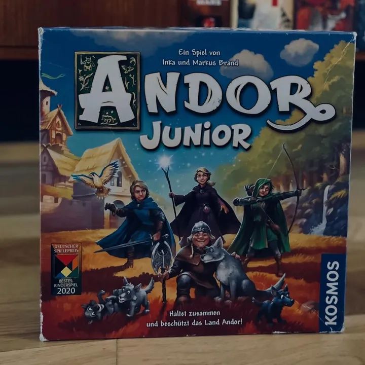 Die deutsche Schachtel von Andor Junior mit Helden und Wölfen auf dem Cover, vor einem Spieleregal