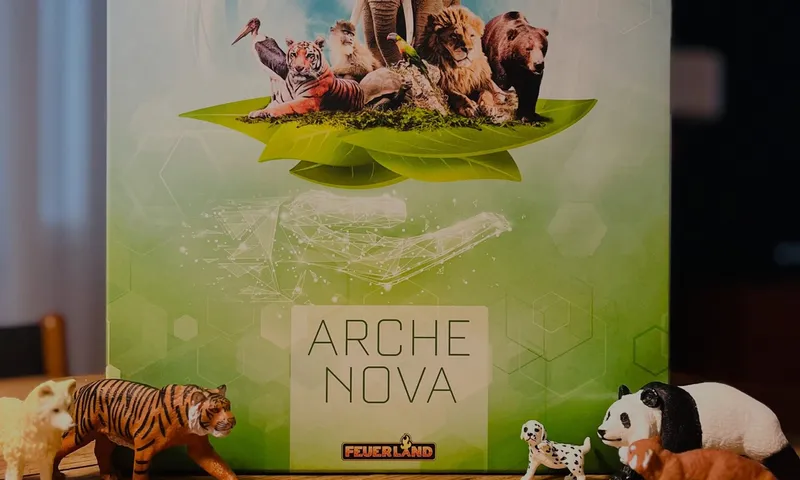 Die Schachtel von Arche Nova auf einem Holztisch, umringt von Spielzeugtieren: ein Tiger, ein Panda, ein Roter Panda und ein Dalmatiner