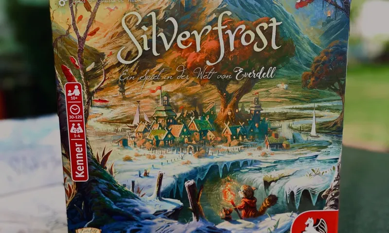 Die Schachtel von Everdell Silverfrost auf einem dunklen Tisch im Freien, Bäume im Hintergrund