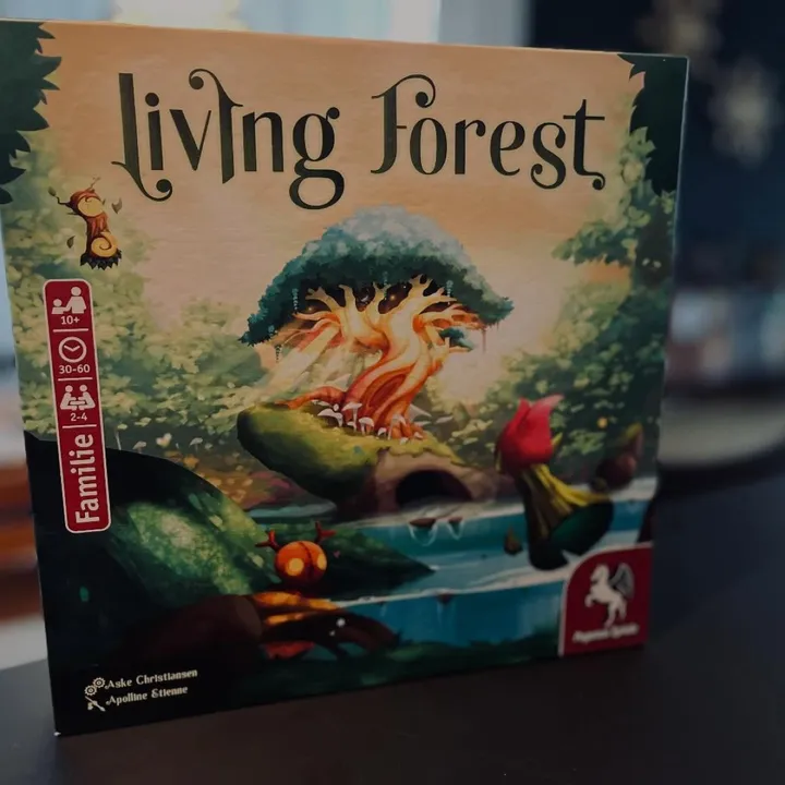 Die deutsche Schachtel von Living Forest mit einem leuchtenden heiligen Baum auf dem Cover, auf einem dunklen Tisch