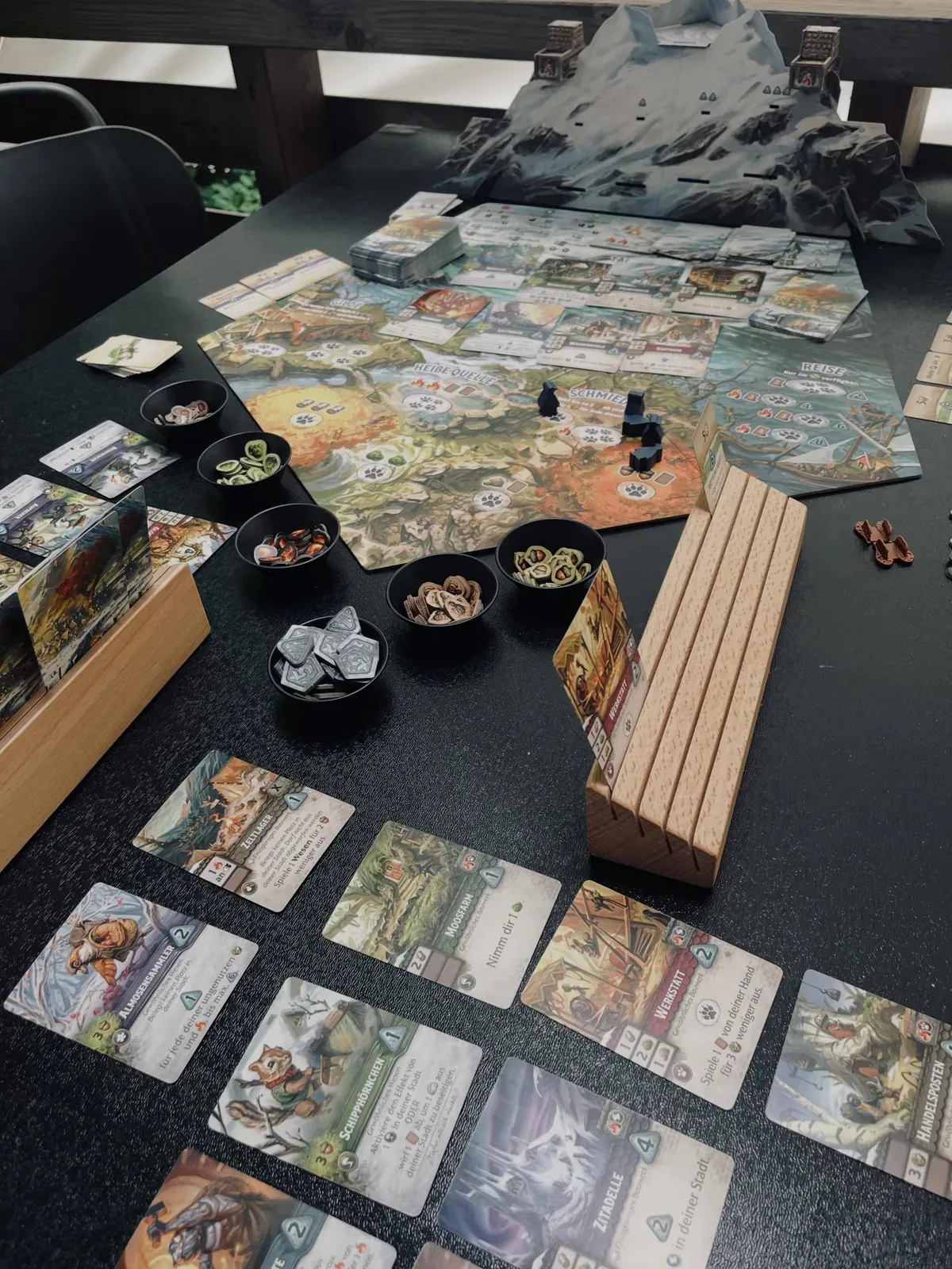 Everdell Silverfrost aufgebaut auf einem dunklen Tisch, mit Bergtableau und Karten