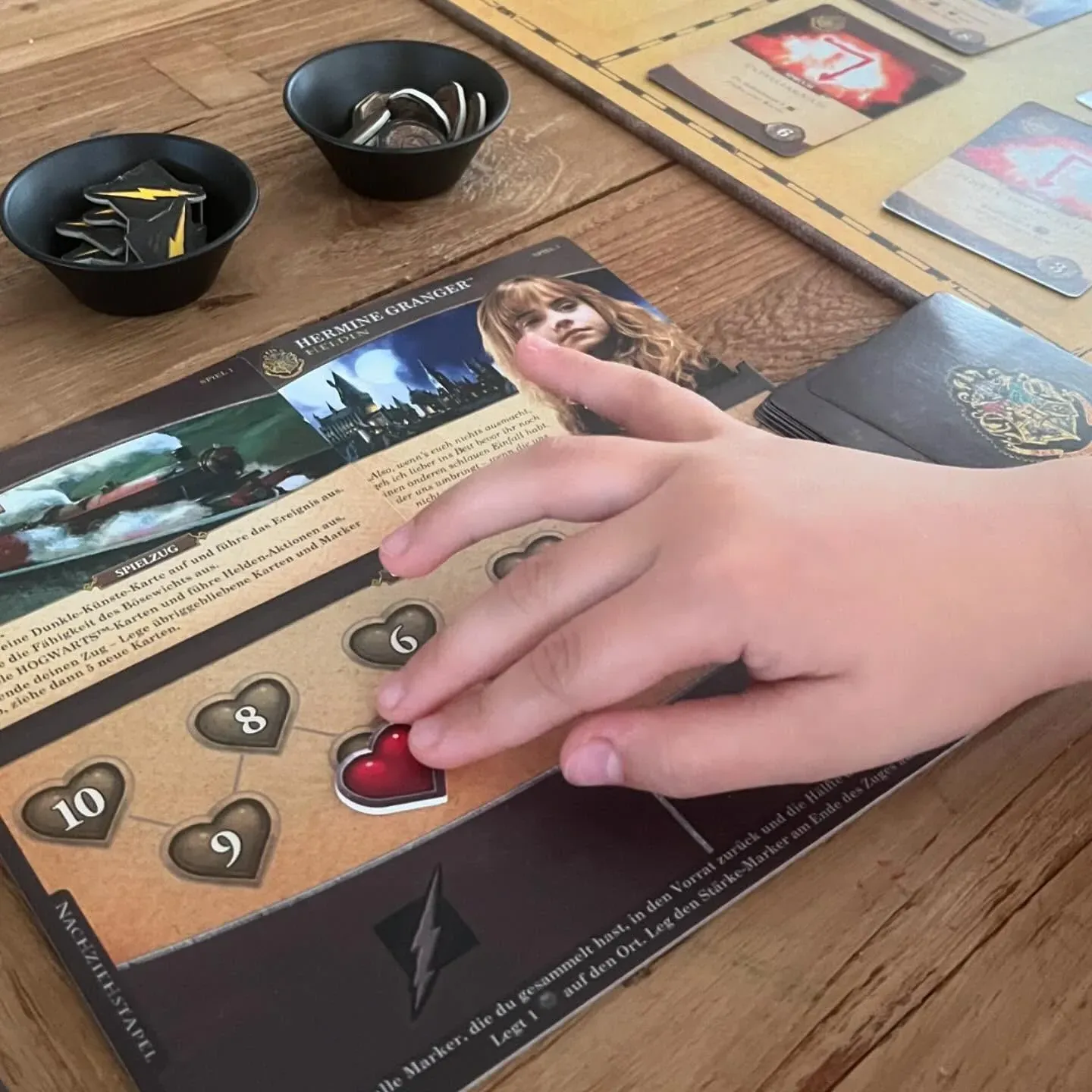 Eine Hand legt einen Marker auf ein Heldentableau von Kampf um Hogwarts