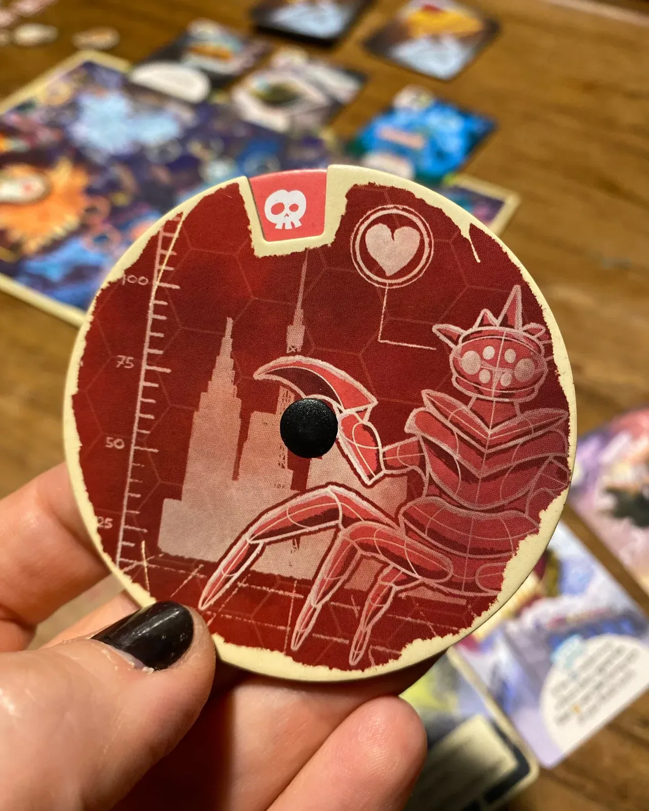 A hand holding a King of Tokyo: Duel token over the board
