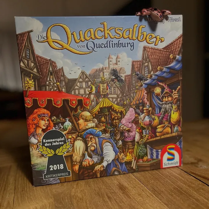 Die deutsche Ausgabe von Die Quacksalber von Quedlinburg auf einem Holztisch, mit dem Kennerspiel-2018-Logo auf der Schachtel
