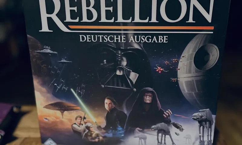 Die Schachtel der deutschen Ausgabe von Star Wars: Rebellion auf einem Holztisch in einem schummrigen Raum