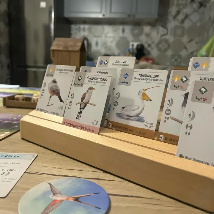 Wingspan bird cards lined up in a wooden card holder on our table